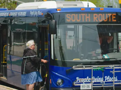 A Midland Penetanguishene Transit Service bus stopped at a curb, displaying “South Route” on the front sign, as a passenger boards through the front door.